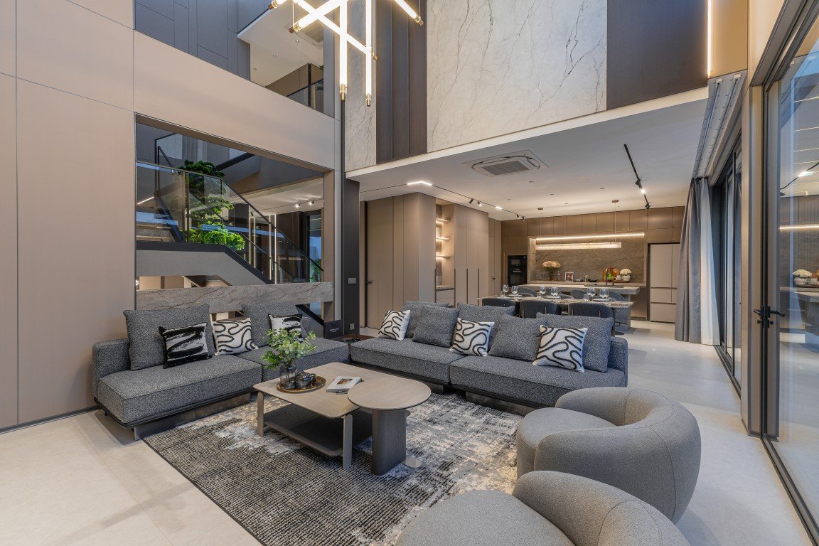Modern open-concept living area with gray sectional sofa, circular and oval coffee tables, and a textured rug in a luxe lounge setting.