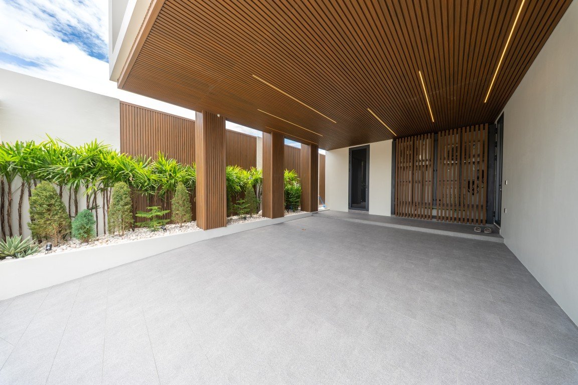 Modern covered patio with a wooden slatted ceiling, vertical brown screens, and a row of tropical plants along a white planter wall.