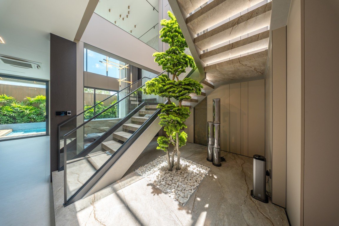 Contemporary two-story lobby with a glass-railed staircase and a tall indoor tree surrounded by white stones.