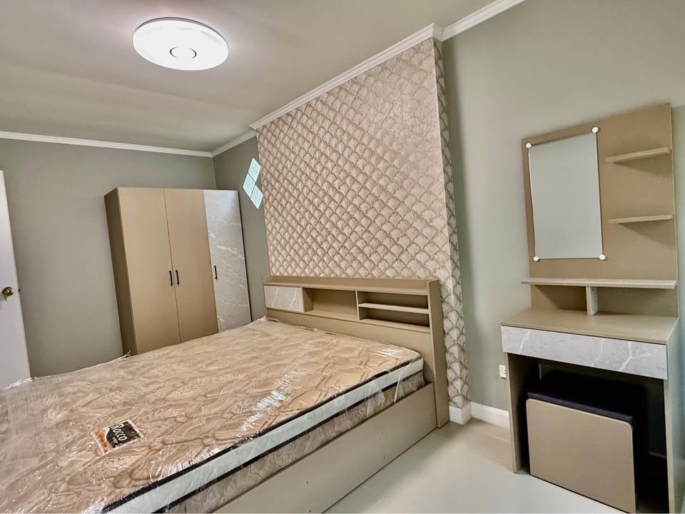 Beige bedroom set with a bed, built-in headboard storage, a tall wardrobe, and a dressing table with mirror against pastel green walls and a patterned feature wall.