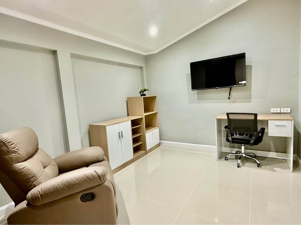 Modern home office setup: desk with chair facing a mounted TV, plus a light wood storage cabinet against a pale wall.