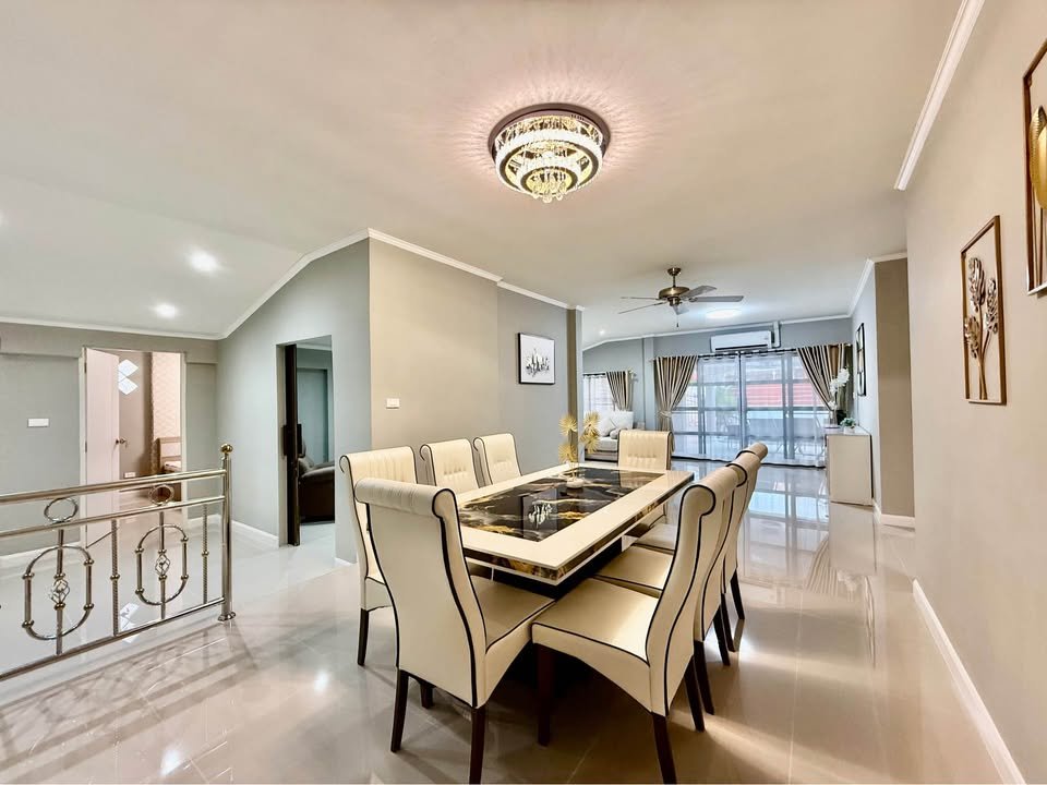 Modern dining room with a long marble-top table and cream upholstered chairs, chandelier overhead, and glossy tiled floor.