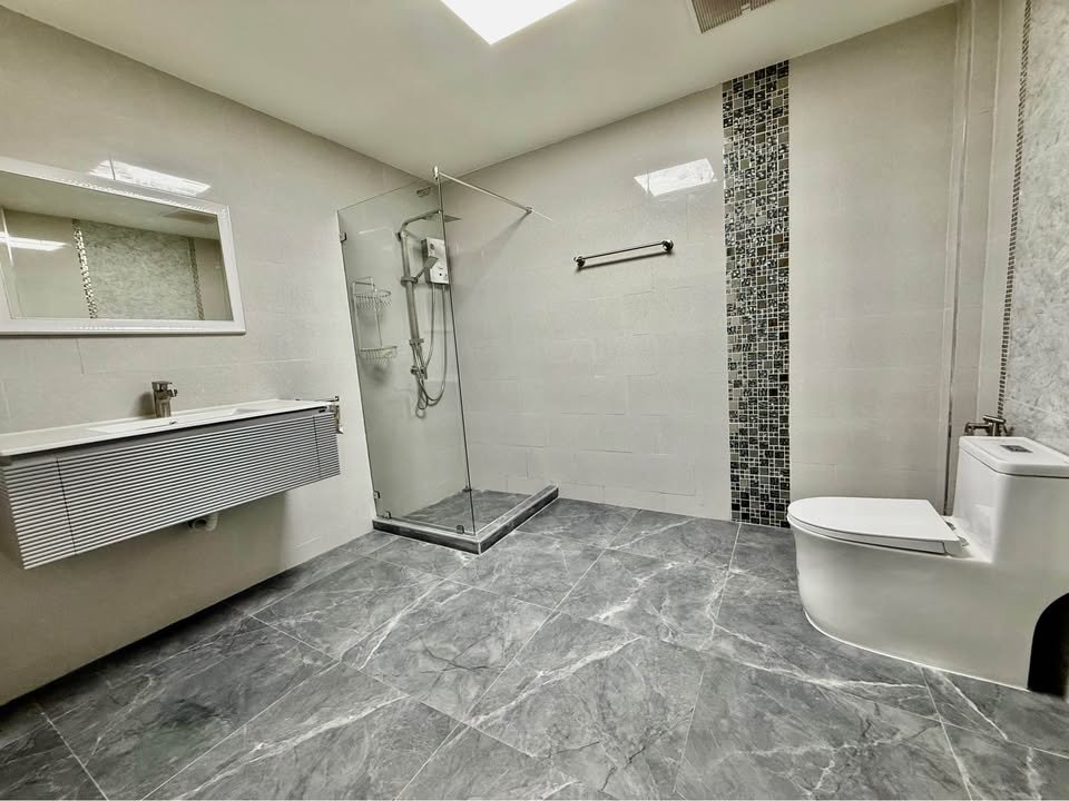 Modern bathroom with glass shower enclosure, wall-mounted sink, large mirror, and white toilet on gray tiled floor.