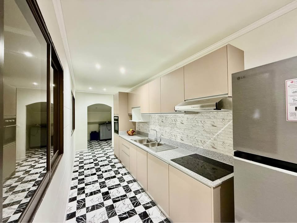 Long modern galley kitchen with beige cabinets, marble backsplash, and a stainless fridge on the right, plus a black-and-white checkered floor.