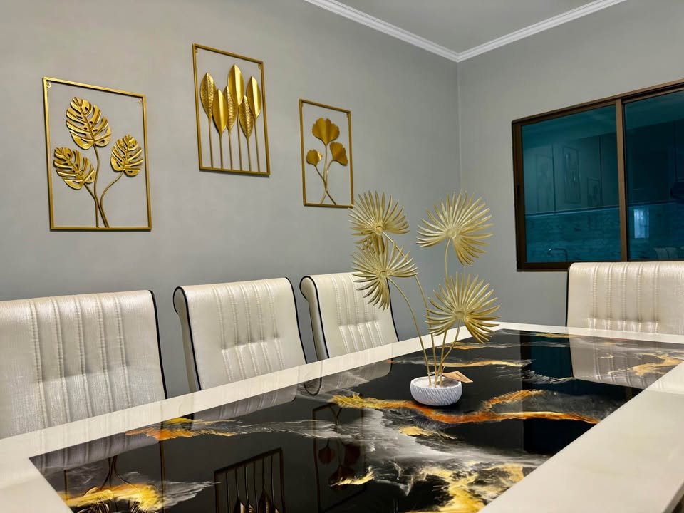 Modern conference room with a glossy black and gold marble table centerpiece and cream padded chairs. Three gold-framed botanical artworks line the gray wall.