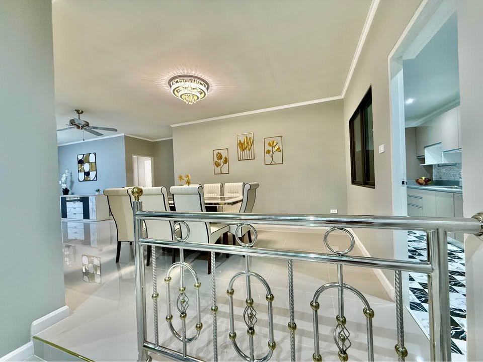 Bright dining room with glass table, cream upholstered chairs, chandelier, and wall art; kitchen visible to the right in an open-plan space.