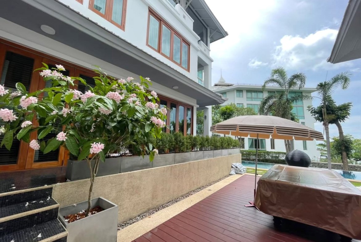 Villa patio with pink flowering shrub in a planter, wooden steps, and a raised garden bed alongside large windows.