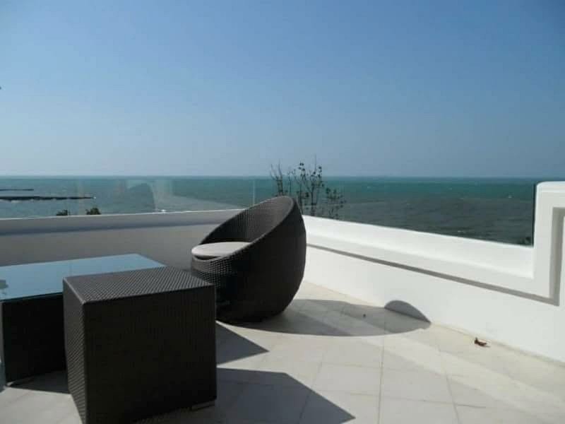 Outdoor balcony with a black wicker round chair and a matching square table, overlooking the sea under a clear blue sky.