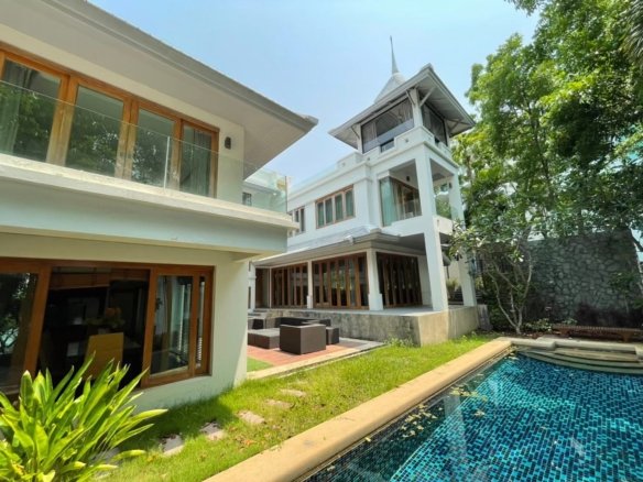 Modern white villa with glass railings wooden framed windows and a blue tiled pool in a sunny garden