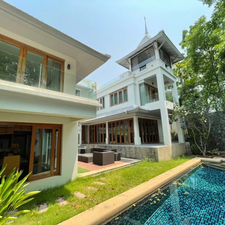 Modern white villa with glass railings wooden framed windows and a blue tiled pool in a sunny garden