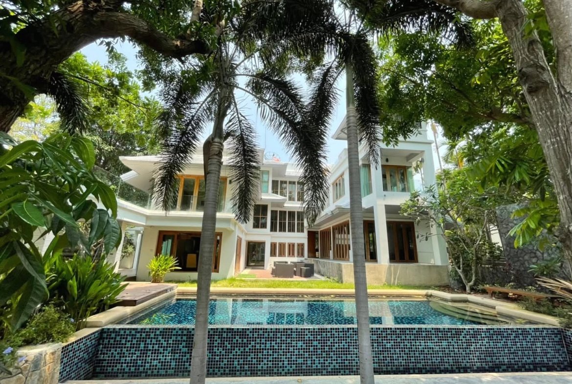 Modern two‑story villa surrounded by palm trees with a blue tiled pool in front.