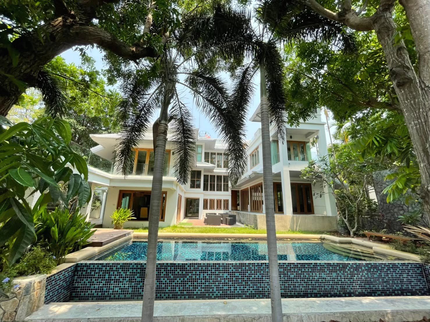Modern two‑story villa surrounded by palm trees with a blue tiled pool in front.