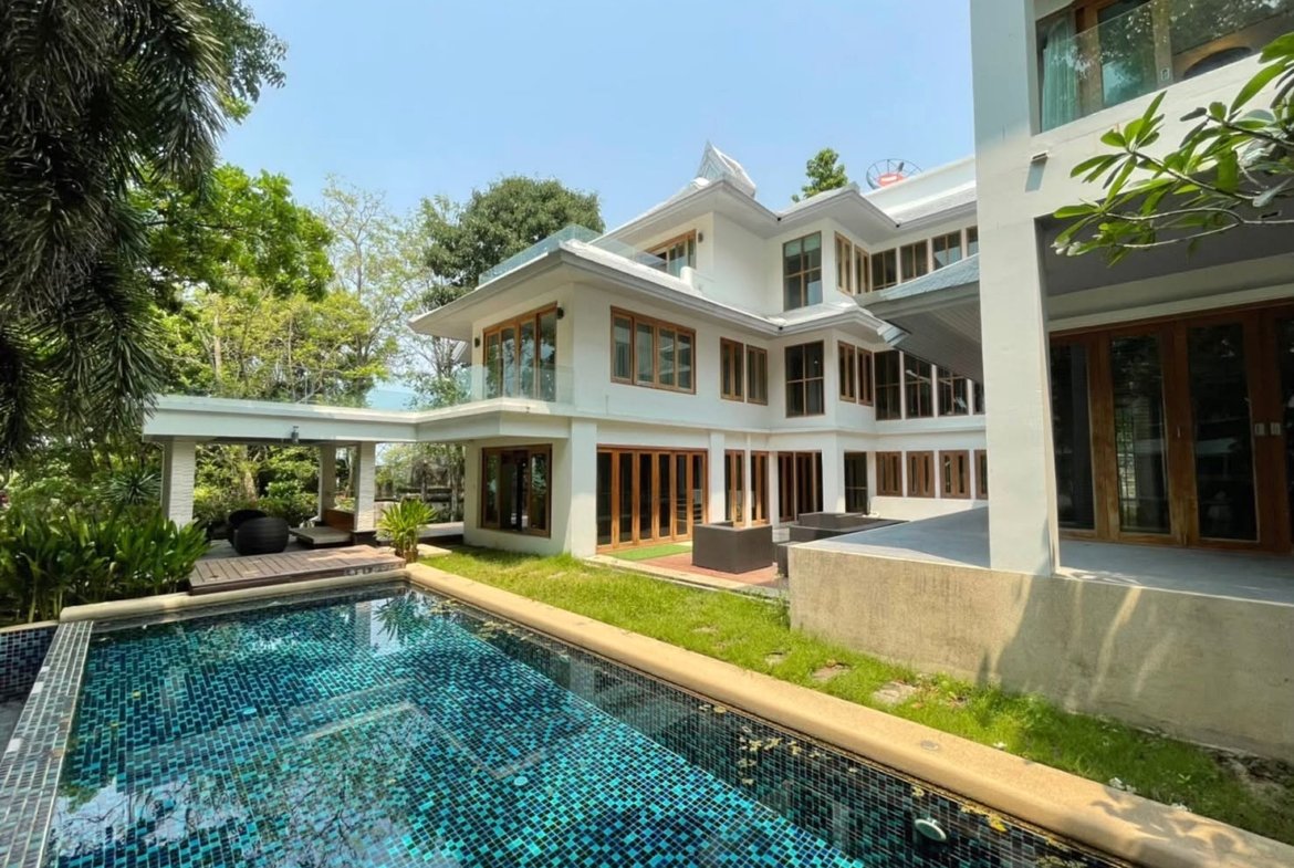 Modern white villa with large glass doors surrounding a rectangular blue-tiled pool and lush greenery.