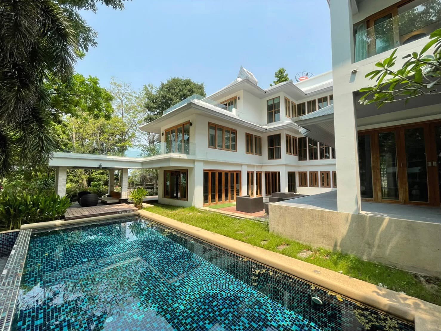 Modern white villa with large glass doors surrounding a rectangular blue-tiled pool and lush greenery.