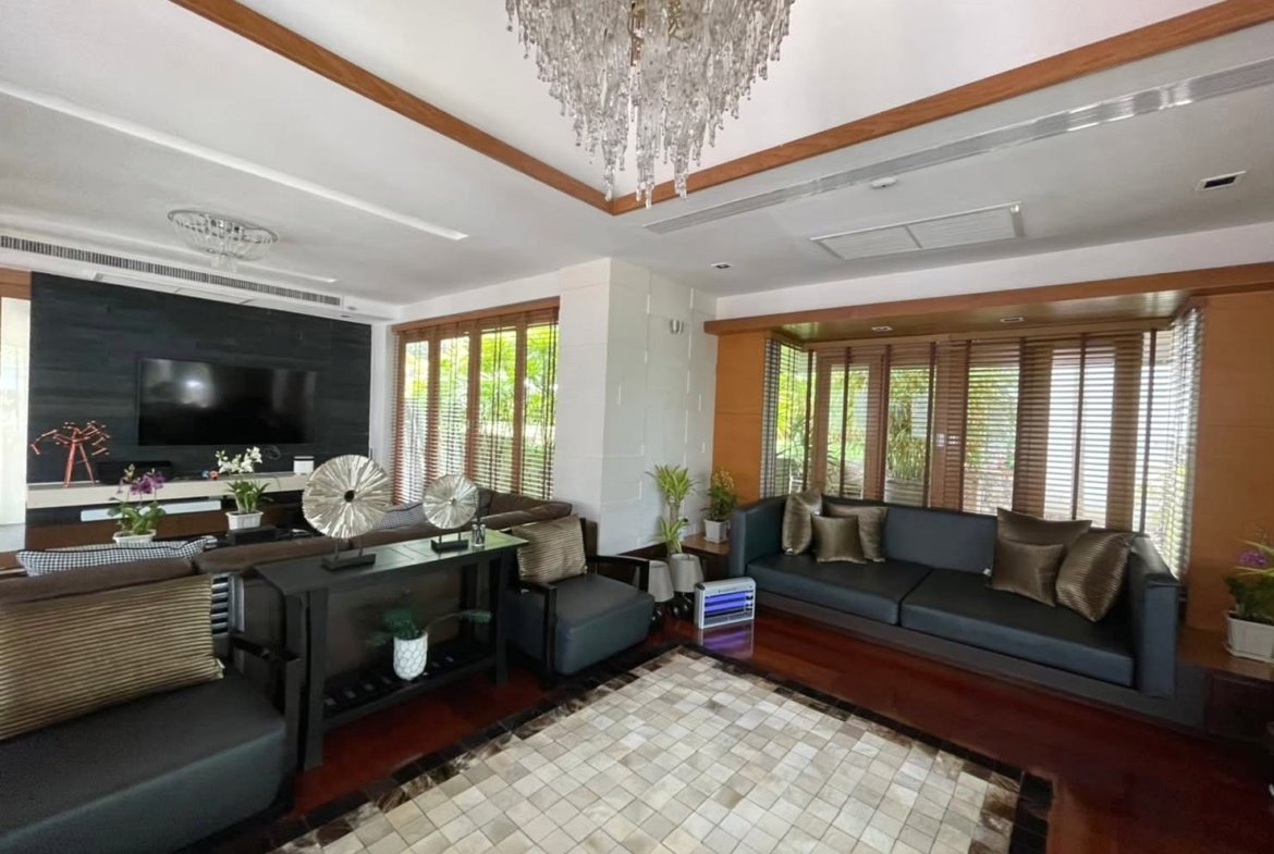 Living room with two dark gray sofas facing a wall-mounted TV on a black accent wall and a crystal chandelier overhead.