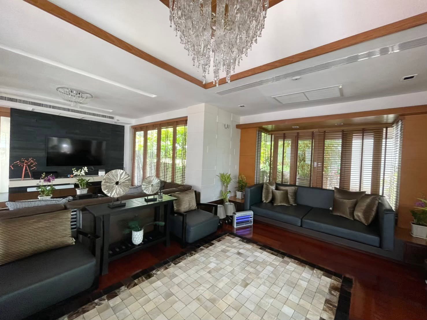 Living room with two dark gray sofas facing a wall-mounted TV on a black accent wall and a crystal chandelier overhead.