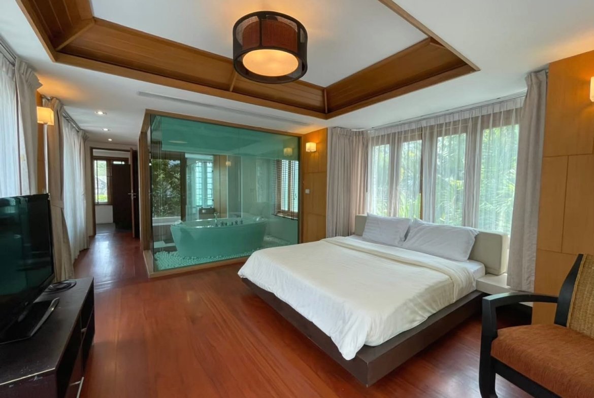Hotel bedroom with a king bed, white linens, and a glass-walled ensuite bathroom with a freestanding tub.