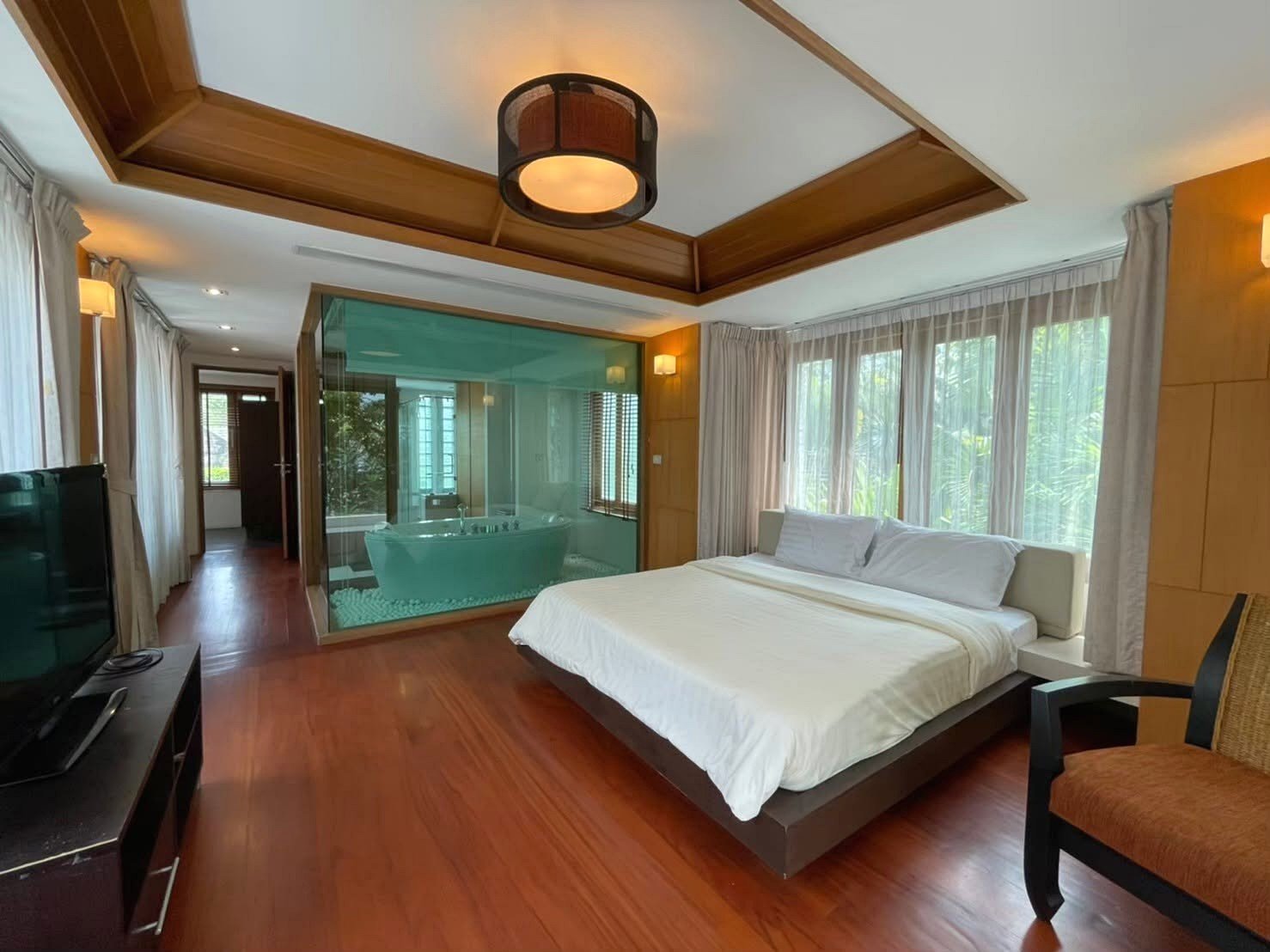 Hotel bedroom with a king bed, white linens, and a glass-walled ensuite bathroom with a freestanding tub.