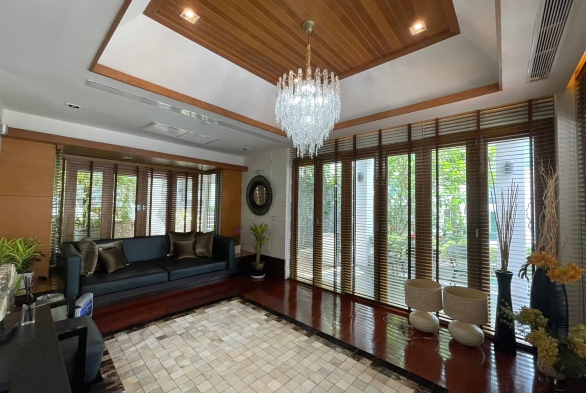 Elegant living room with crystal chandelier, wood-paneled ceiling, and a blue sectional sofa by large windows.