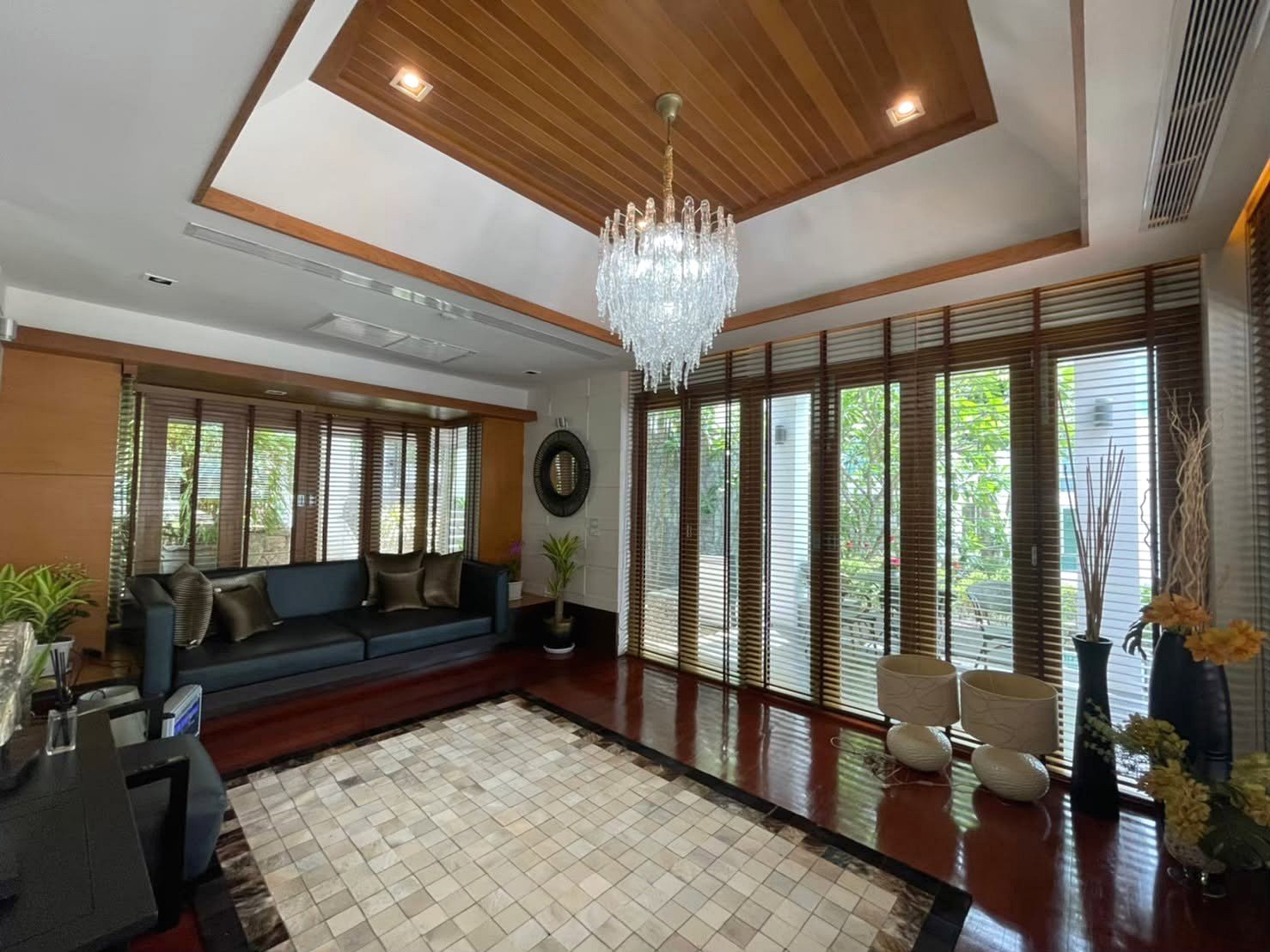 Elegant living room with crystal chandelier, wood-paneled ceiling, and a blue sectional sofa by large windows.