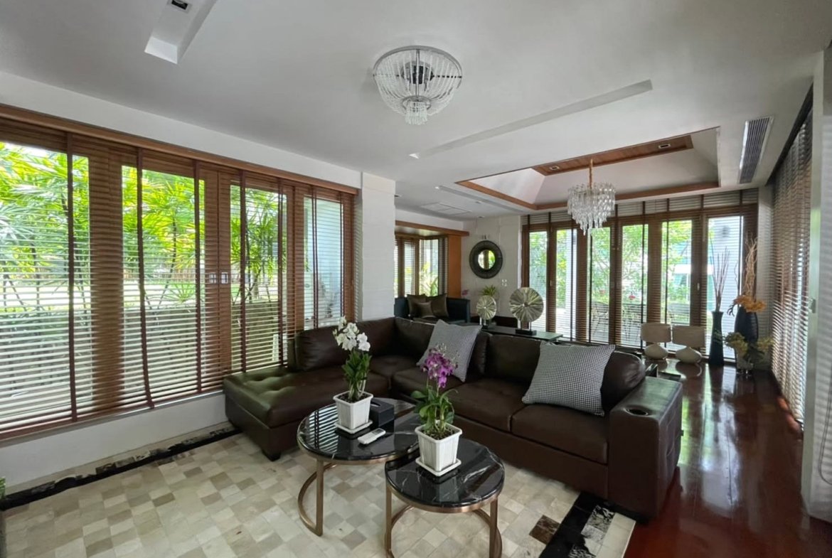 Spacious living room with a dark brown leather sectional, two glass coffee tables, and potted orchids on white pots.