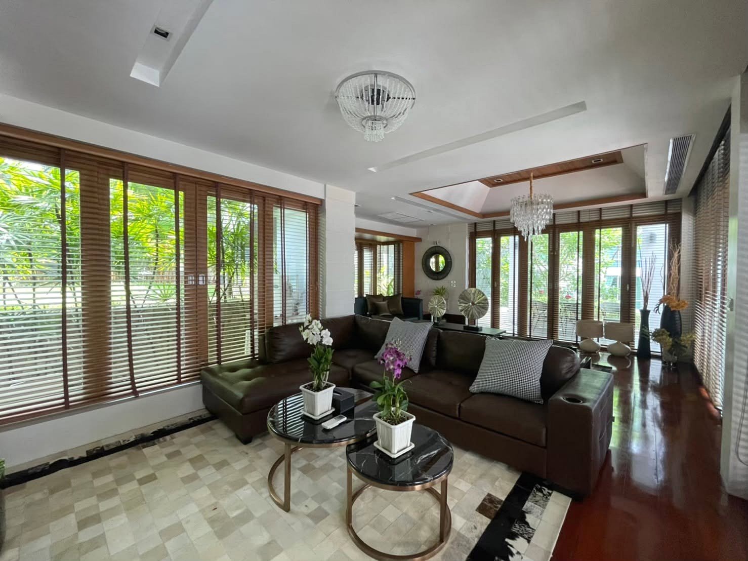 Spacious living room with a dark brown leather sectional, two glass coffee tables, and potted orchids on white pots.