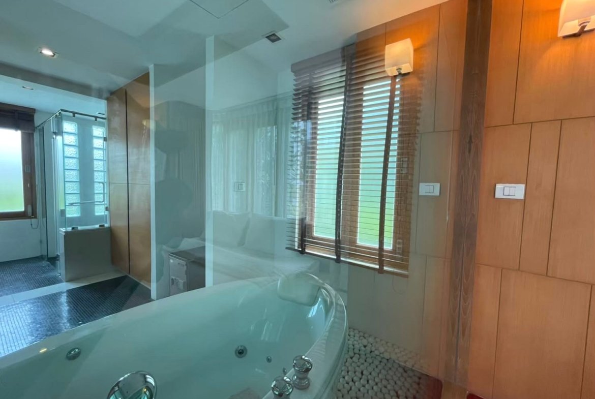 Modern bathroom with a large white jetted tub, glass divider, and pebble floor near a wooden panel wall.