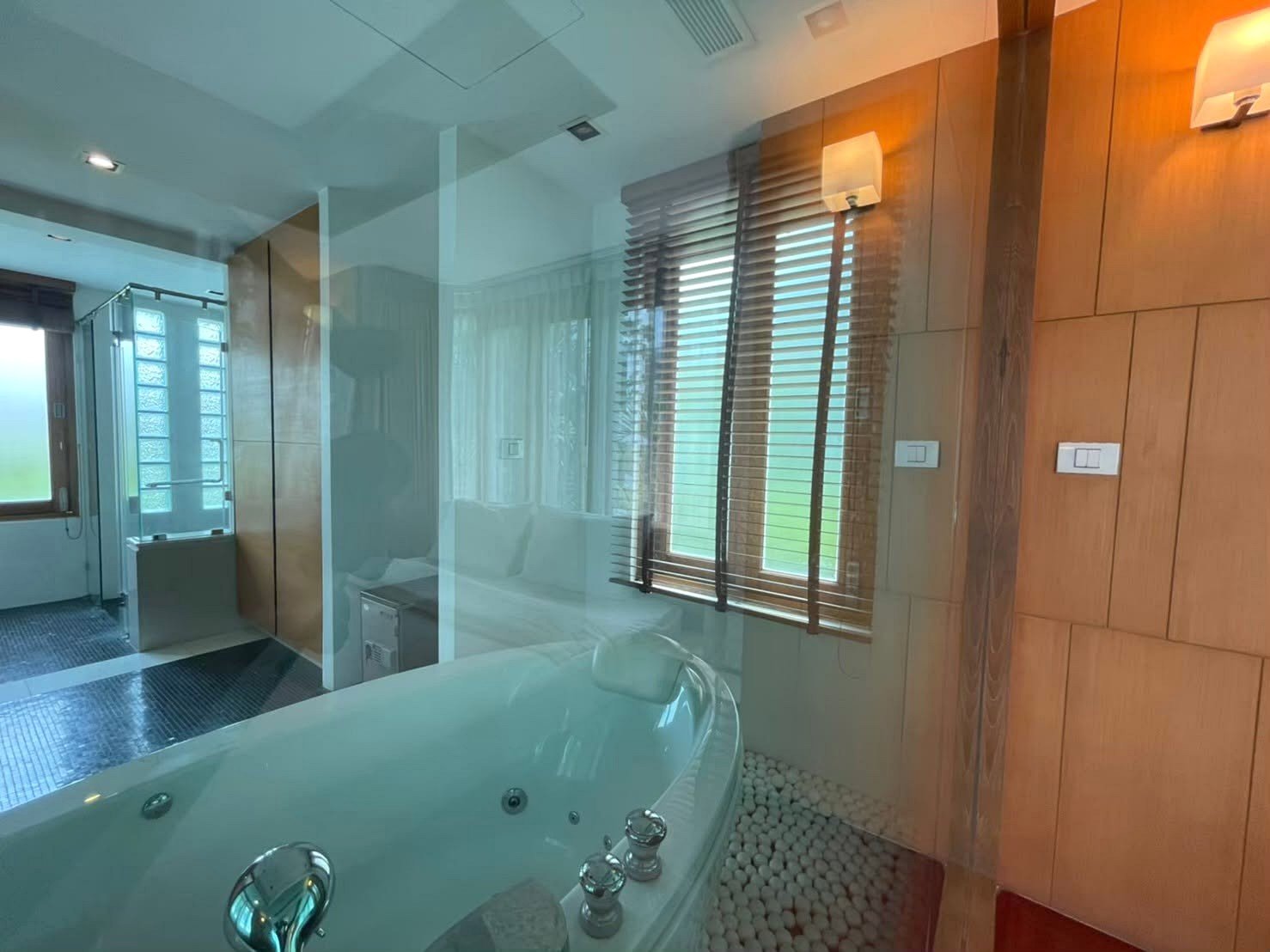 Modern bathroom with a large white jetted tub, glass divider, and pebble floor near a wooden panel wall.