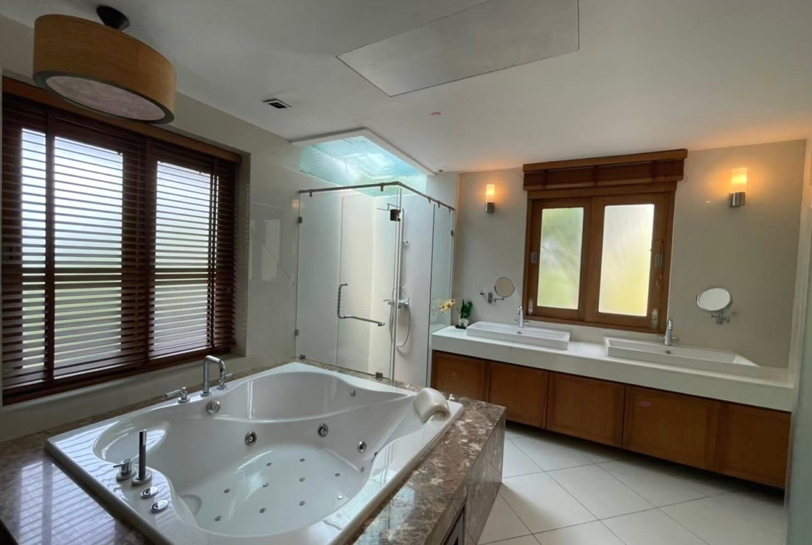 Luxurious bathroom with a large jetted tub in the foreground, a glass-enclosed shower to the left, and a double sink vanity under a wooden-framed window.