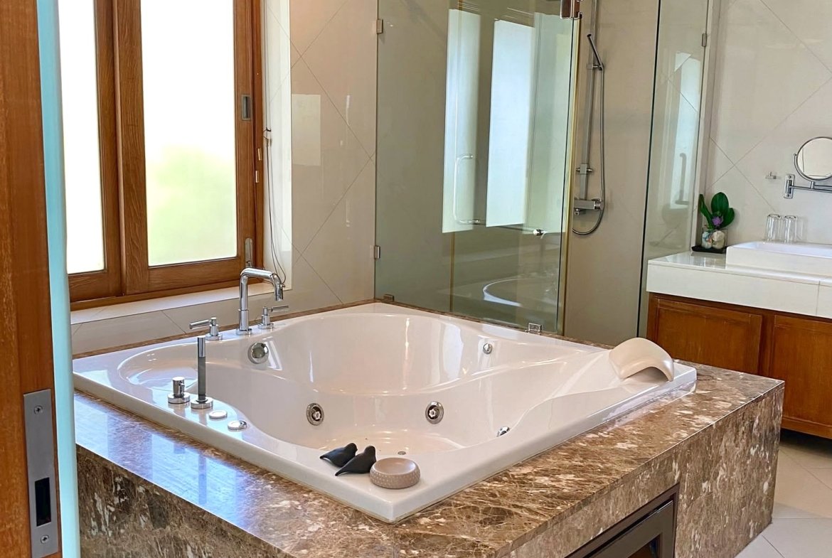 Luxurious bathroom with a large oval jacuzzi tub set in a marble surround and a glass-walled shower behind it.
