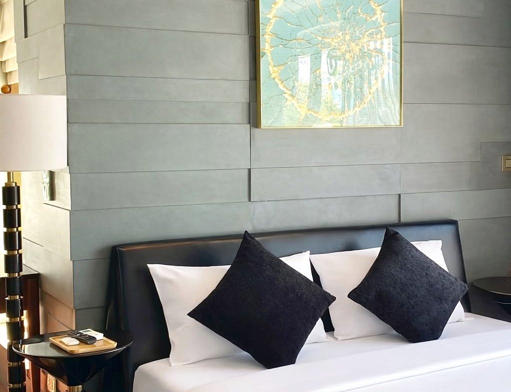 Hotel bedroom with a gray paneled accent wall, framed art above a white bed with three black accent pillows.