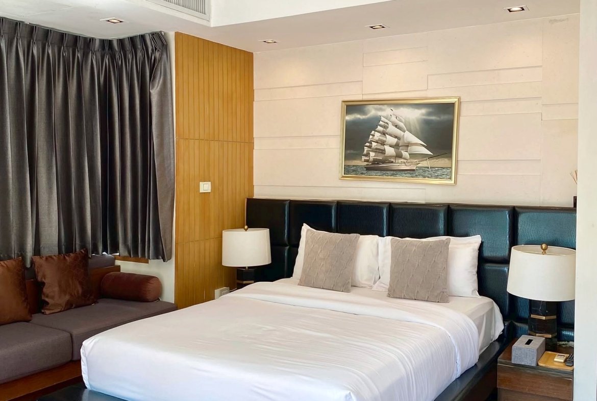 Hotel bedroom with a king bed, white linens, dark headboard, and nautical artwork above the bed.