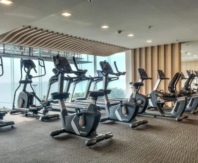 Row of treadmills and stationary bikes in a bright modern gym with large windows.